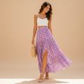 A woman models a white spaghetti-strap crop top and a high-slit, lavender-purple floral print maxi skirt, holding a woven straw handbag against a solid beige studio backdrop.